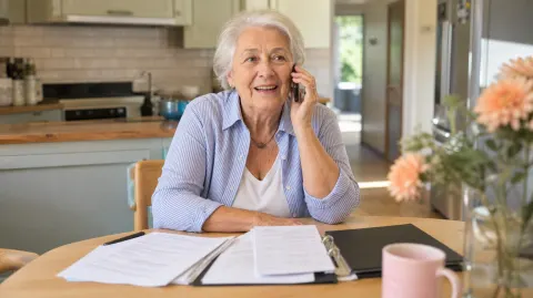 An older woman on the phone with a folder of paperwork