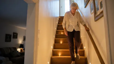 A woman walking down a well-lit staircase holding the handrail